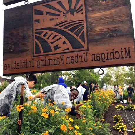 small group of volunteer serving in a garden under a Michigan Urban Farming Initiative sign 